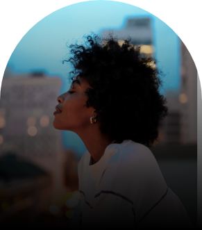 A side profile of a Black woman with afro hair wearing a white jumper. Her eyes are closed.